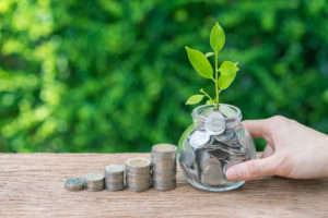 Hand holding jar with full of coins with growth sprout plant as financial investment concept.