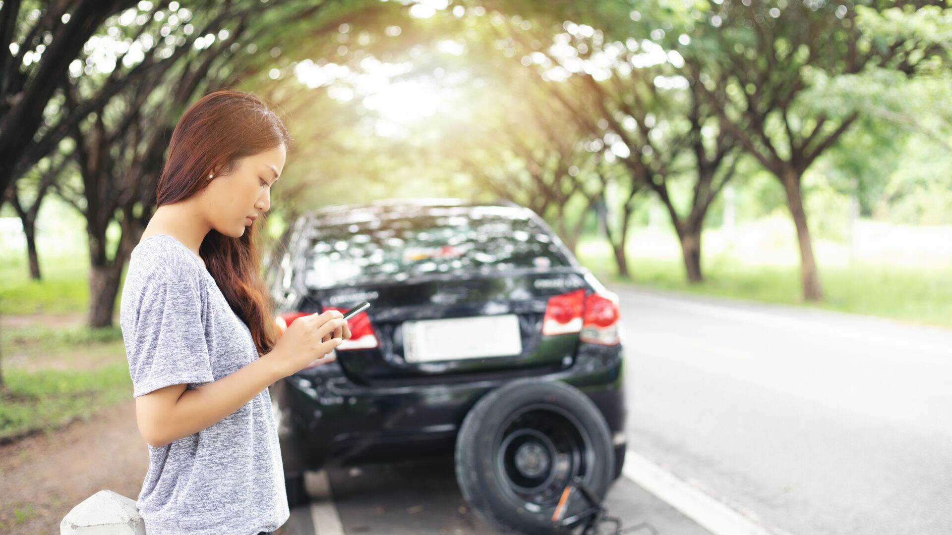 Women standing on the side of the road on her phone, next to a car.