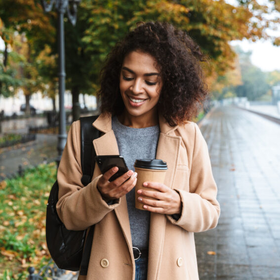 Woman walking and scrolling on phone with coffee.