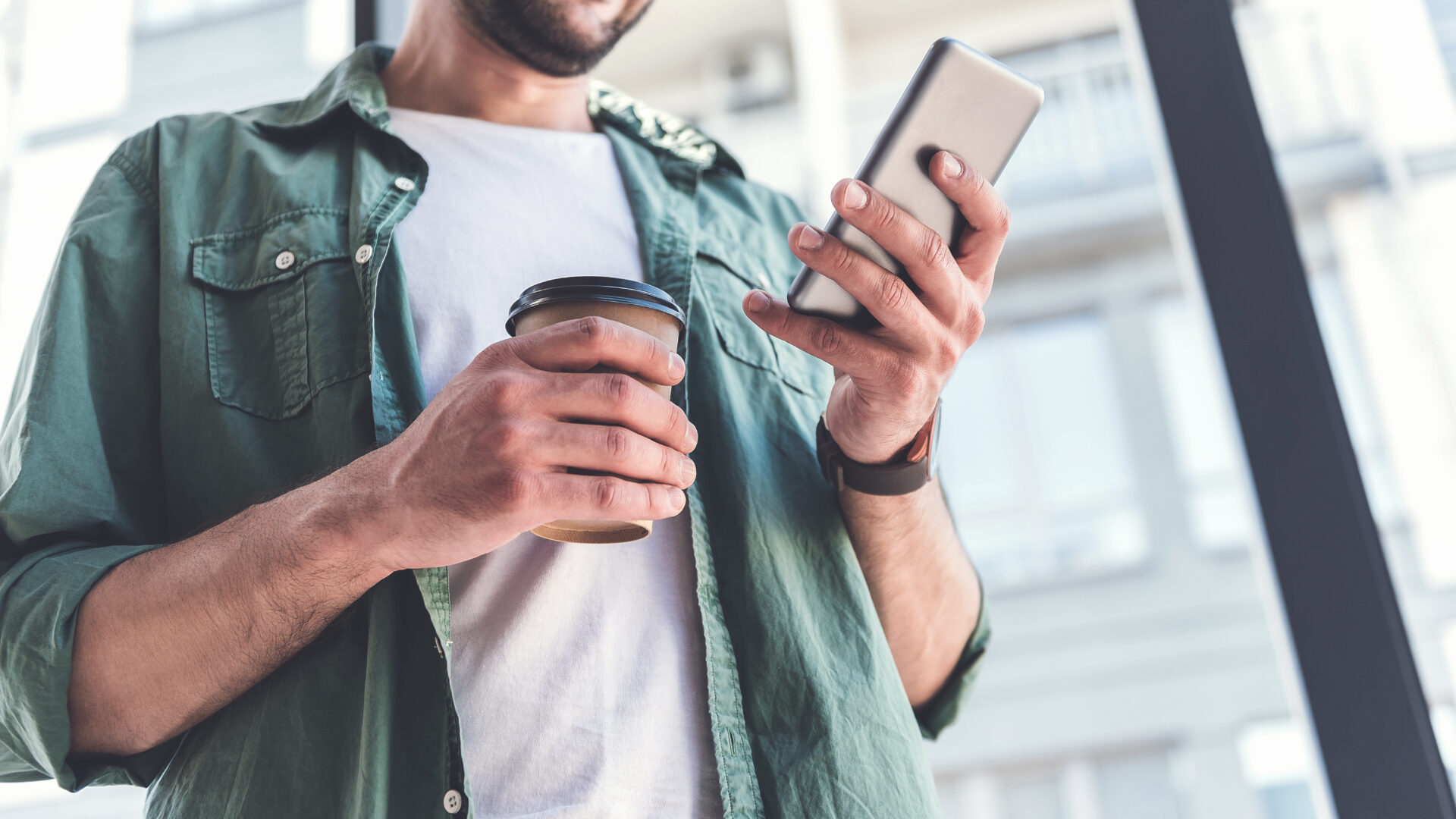 Man holding a coffee and scrolling on a smartphone.