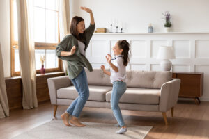 Adult female and child dancing in living room.