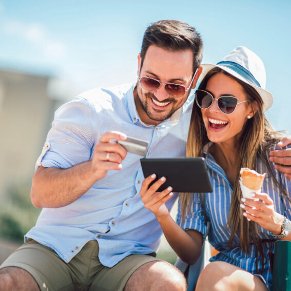 Couple eating an ice-cream phone while looking at a tablet, and holding a credit card.