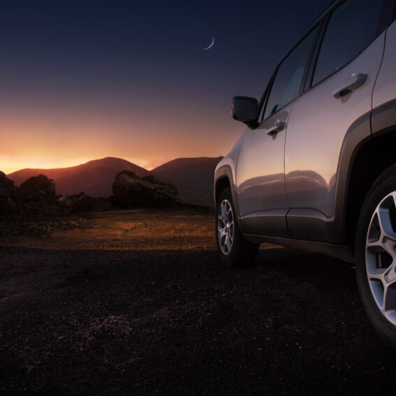 Side profile of an SUV by the mountains and the sun setting.